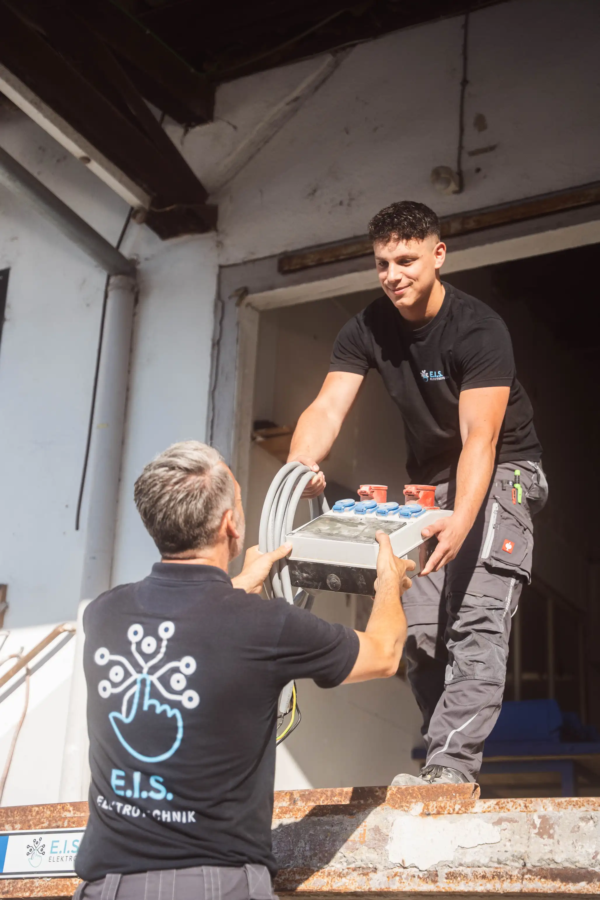Zwei Monteure heben einen Verteiler an — E.I.S. Elektrotechnik